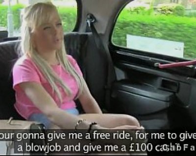 A blonde bimbo wearing a pink shirt sits in a black car.