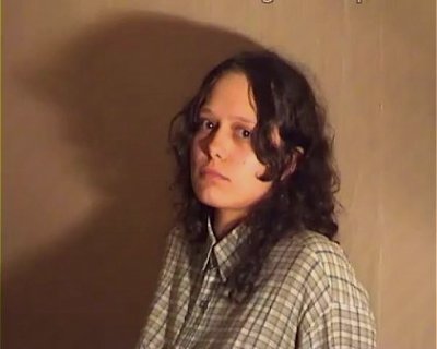 A girl named Russian Whip posing in front of a wall with brown trim.