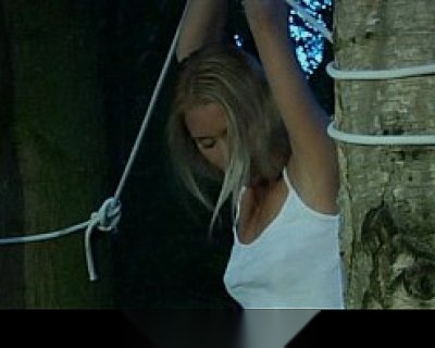 A beautiful blonde bimbo is tied to a tree and experiencing discomfort.