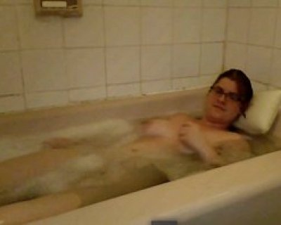 A beautiful whore wearing glasses lays in a tub full of soapy water. Prjv