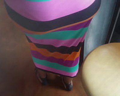 A person wears a multicolored striped dress in a room with a colorful striped chair. Soxcub91
