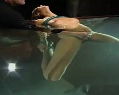 The bimbo is submerged in a body of water while her trainer adjusts her foot.