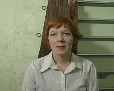 A lady with red hair and a white shirt is smiling at the camera.