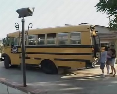 A male is getting onto a yellow bus. It is pulling up to a stop.