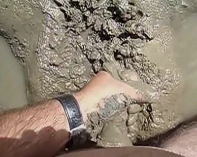 A male's hand is deep in mud.
