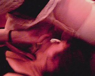 A person bends over near a bed. The person is wearing black clothes.