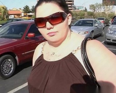 A bimbo in a brown dress is walking on the street with a black purse.